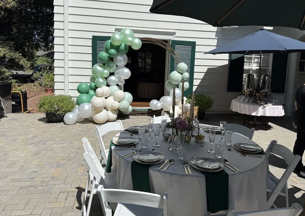 Sage and white balloon arch over an arched doorway paired with a styled tablescape — balloon and floral styling for Tracy and Manteca celebrations