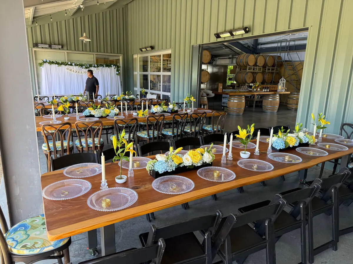 Winery table lined with yellow lily, blue hydrangea and white rose centerpieces between taper candles — centerpiece design for Tracy and Modesto receptions