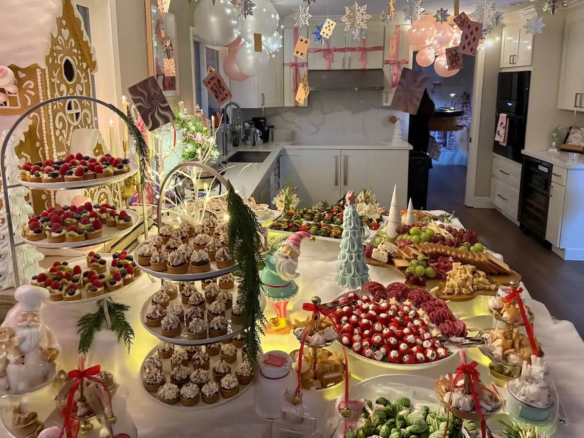 Whimsical Alice in Wonderland themed appetizer and dessert tablescape with tiered fruit tarts, cupcakes, charcuterie, caprese skewers, and pastel balloon and playing card decor by Tracy Catering Company